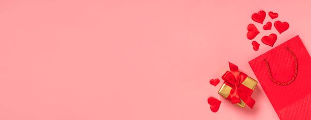 Červený papírový sáček, červená srdce a dárková saténová stuha luk růžové pozadí. Slavnostní pozadí Valentines den - Fotografie, Obrázek