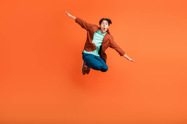 Full size photo of smiling guy jumping fooling around hands wings plane fly isolated on orange color background - Foto, imagen