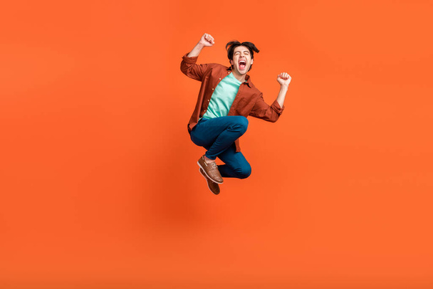 Full size photo of excited crazy smiling male jumping raise fists in victory triumph isolated on orange color background - Foto, Bild