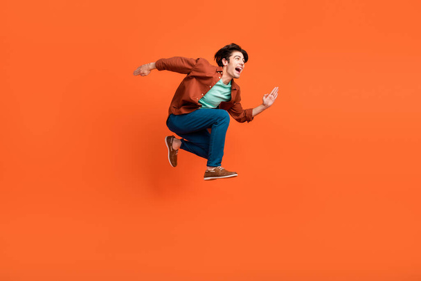 Foto lateral de perfil de tamanho completo de homem funky feliz correndo no ar olhar copyspace viajando isolado no fundo cor de laranja - Foto, Imagem