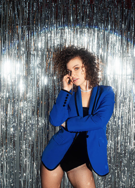  curly haired woman in blue jacket posing on sparkling disco background  - Foto, Imagen