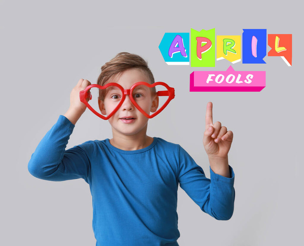 Lustiger kleiner Junge mit großer herzförmiger Brille und erhobenem Zeigefinger auf hellem Hintergrund. Feier zum Aprilscherz - Foto, Bild