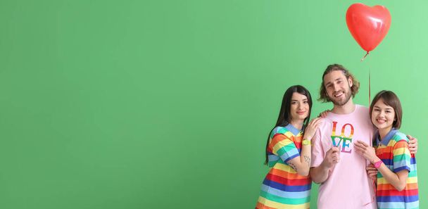 Mann und zwei schöne Frauen in Regenbogenkleidung, mit Wort LIEBE und Luftballon auf farbigem Hintergrund mit Platz für Text. Konzept der Polyamorie und LGBT - Foto, Bild