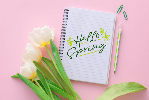 Notebook szöveggel HELLO SPRING, fehér tulipán virágok és írószer rózsaszín alapon - Fotó, kép