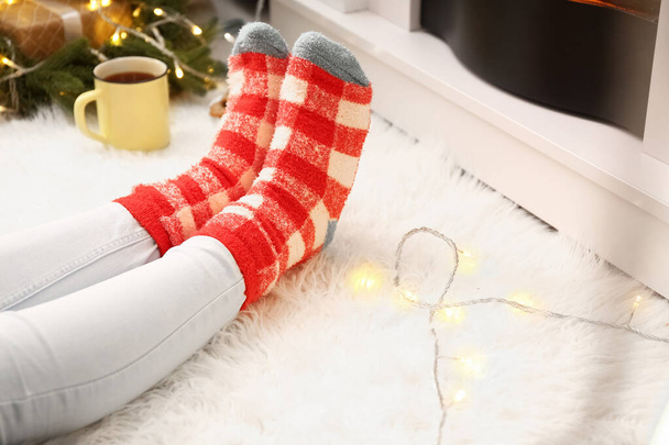 Γυναίκα με ζεστές κάλτσες κοντά στο τζάκι στο σπίτι την παραμονή των Χριστουγέννων, κοντινό πλάνο - Φωτογραφία, εικόνα