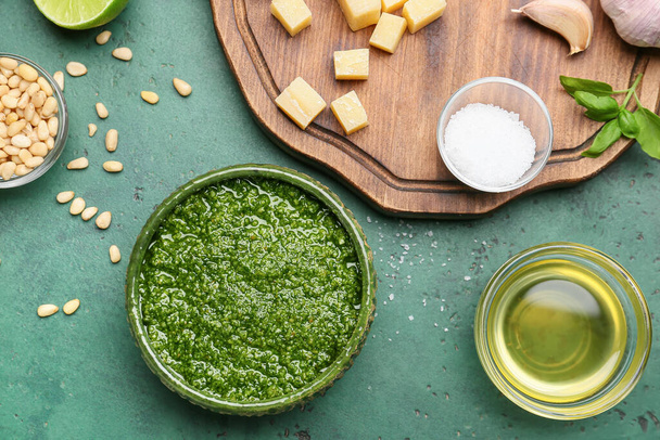 Bowl of tasty pesto sauce and ingredients on green background - Zdjęcie, obraz