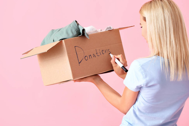 Молода жінка з коробкою пише слово DONATIONS на рожевому фоні
 - Фото, зображення