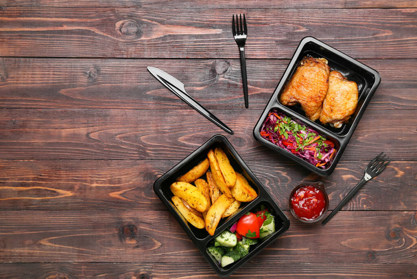 Takeaway boxes with tasty food, bowl with sauce and cutlery on wooden background - Photo, Image