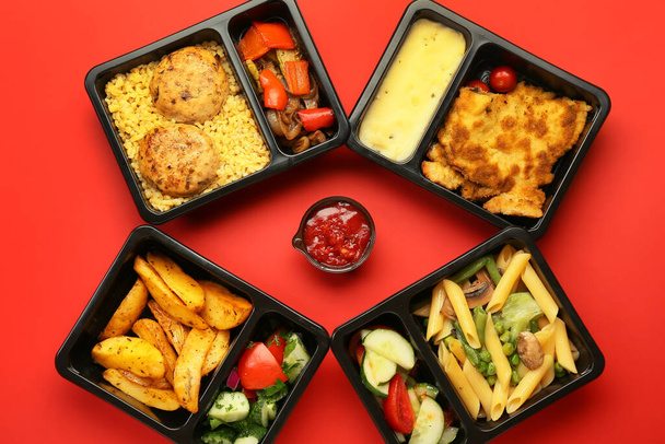 Lunch boxes with delicious food and bowl with sauce on color background - Photo, Image