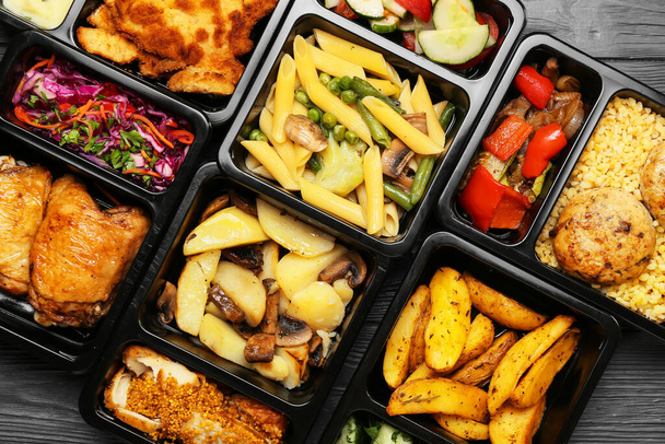 Cajas de almuerzo con diferentes sabrosos alimentos sobre fondo de madera gris, primer plano - Foto, Imagen