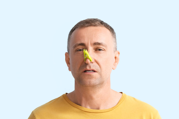 Ill volwassen man met wasknijper op zijn neus tegen kleur achtergrond - Foto, afbeelding