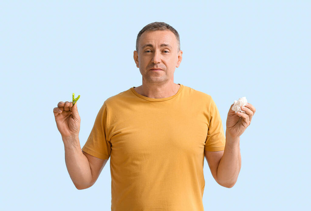 Volwassen man met wasknijper en weefsel op kleur achtergrond. Stom neusconcept - Foto, afbeelding