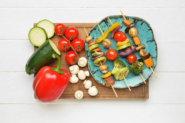 Board with tasty vegetable skewers on light wooden background - Фото, изображение
