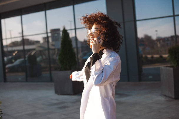 Caucasian curly haired woman freelancer talking on phone having conversation with friends. Mobile communication. Side view. - Фото, зображення