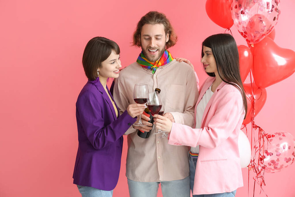 Hombre y dos hermosas mujeres bebiendo vino sobre fondo de color. Concepto de poliamory y LGBT - Foto, imagen