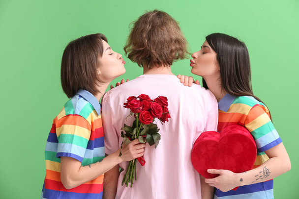 Erkek ve iki güzel kadın gökkuşağı kıyafetleri içinde, hediyeleri ve renkli arka planda çiçekleri var. Çokeşlilik ve LGBT kavramı - Fotoğraf, Görsel