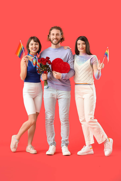 Man en twee mooie vrouwen met regenboog vlaggen, cadeau en bloemen op kleur achtergrond. Begrip polyamorf en LGBT - Foto, afbeelding