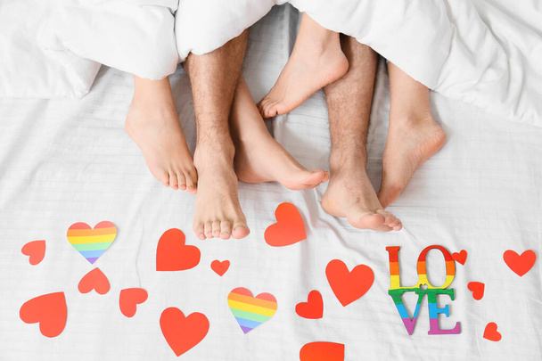 Fiatal férfi és két nő lábai az ágyban, papírszívvel borítva, felülnézetből. A poliamória és az LMBT fogalma - Fotó, kép