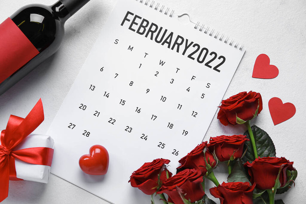 Calendar with bottle of wine, gift, hearts and roses on white background. Valentine's Day celebration - Photo, Image