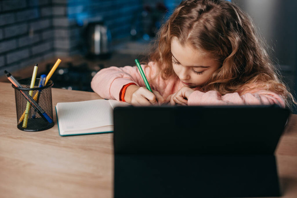 家に座っている間に小さな女の子が勉強し、デジタルタブレットを使用してノートを取る. - 写真・画像