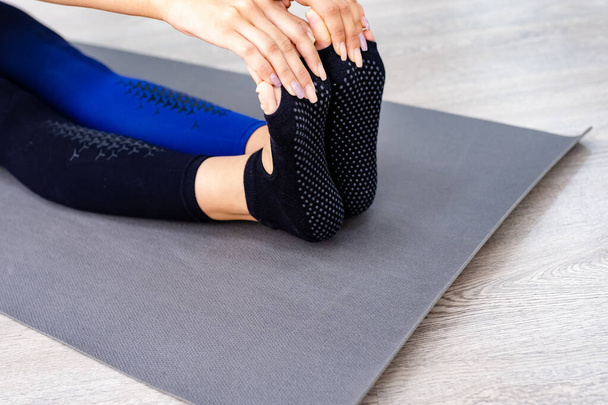 Gros plan Vue du dessus des mains tenant le pied d'une femme assise sur un tapis de yoga à l'extérieur sur un plancher de bois - Photo, image