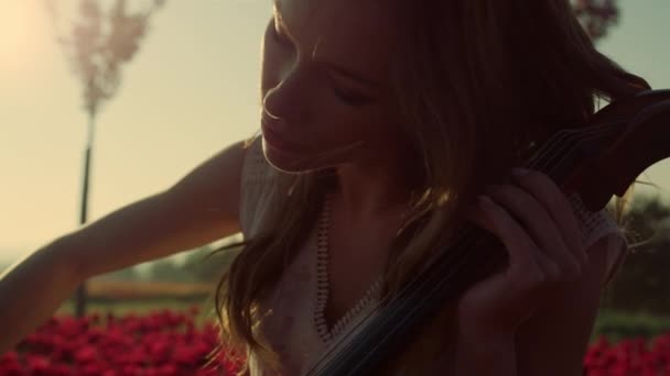 Крупный план вдохновил молодую женщину играть на виолончели в цветущем летнем саду на открытом воздухе. - Кадры, видео