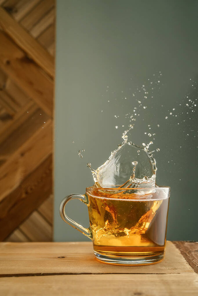 Transparent mug with tea and splashes on a green background. - Photo, image