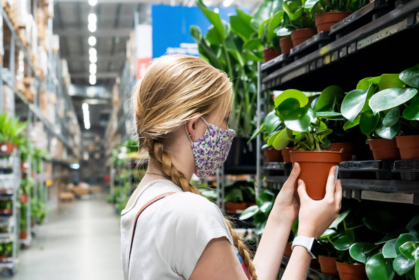 New normal retail shopping. A girl wearing face mask choosing potted plants in retail garden warehouse store. Covid-19 pandemic - Photo, Image