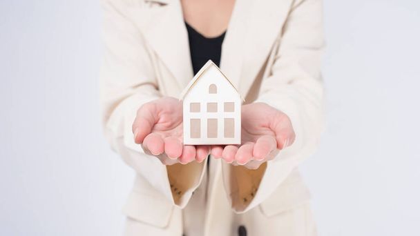 Young beautiful woman in suit holding small model house over white background studio - Photo, Image