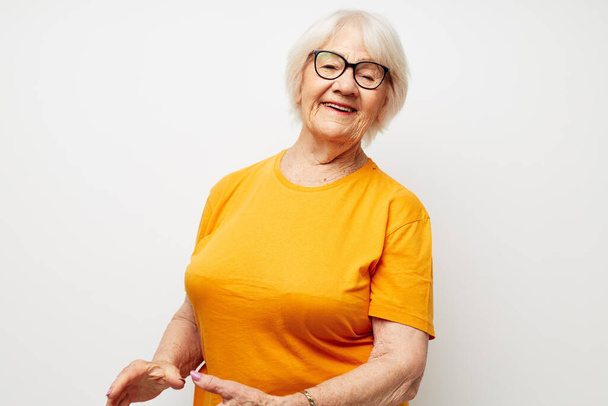 Portrait of an old friendly woman in casual t-shirt and glasses light background - Фото, изображение