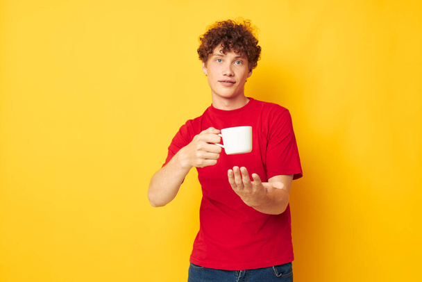 guy with red curly hair white mug in the hands of a drink yellow background unaltered - Valokuva, kuva