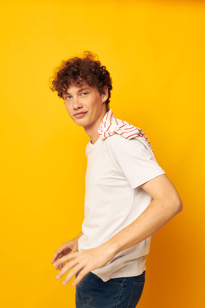 guy with red curly hair in a white t-shirt holds a striped t-shirt fashion youth style yellow background unaltered - Photo, Image