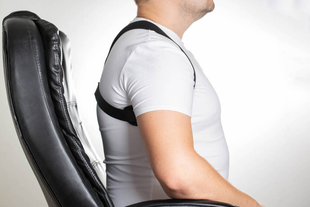 A male is wearing an orthopedic posture corrector. Treatment for stoop and back problems - 写真・画像
