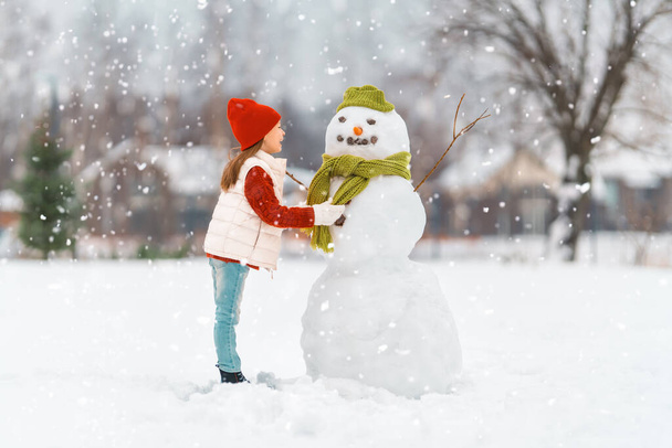 Happy child girl playing with a snowman on a winter walk in nature - Foto, Bild