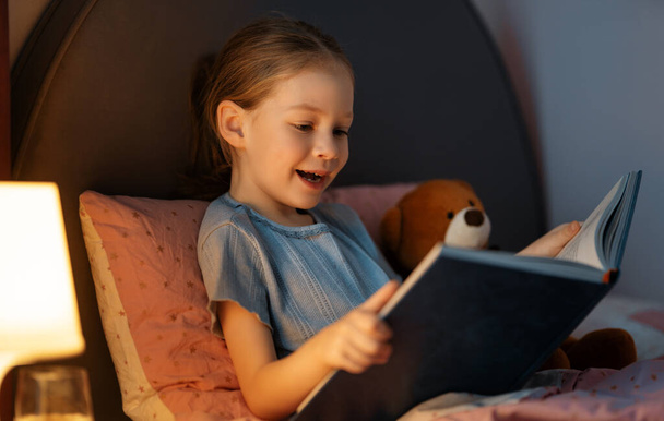 Cute little girl is reading a book in her bedroom. - Fotoğraf, Görsel