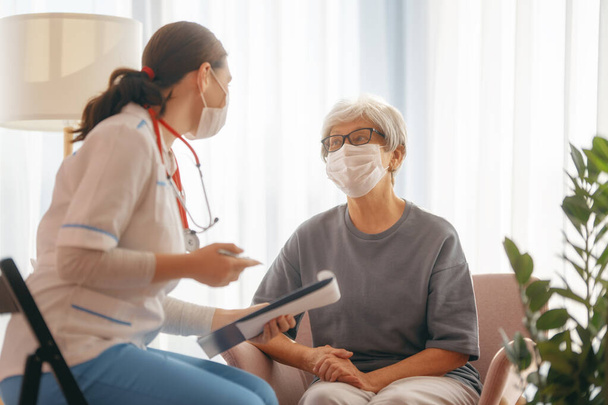 Doctor and senior woman wearing facemasks during coronavirus and flu outbreak. Virus protection. COVID-2019. Taking on masks. - Foto, Bild