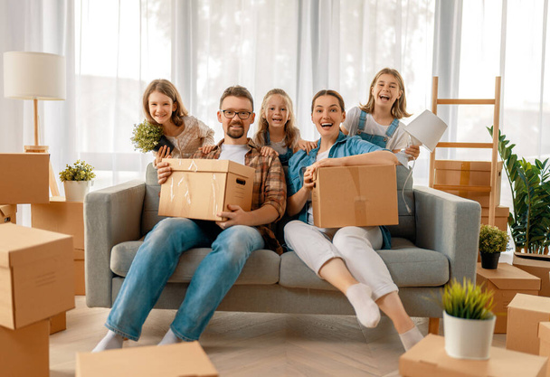 Happy young family are moving to new apartment. Parents and daughters with boxes. - Photo, Image