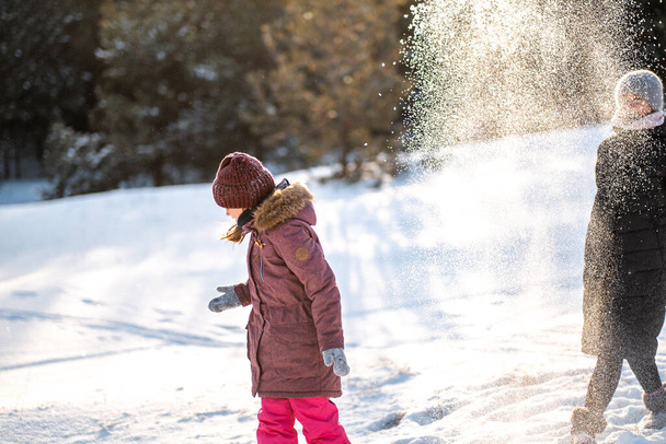 Kışın aktif aile tatili. Anne ve kızı izin günlerinde ormanda eğlenirler. Annesiyle parktaki karda oynayan bir kız.. - Fotoğraf, Görsel