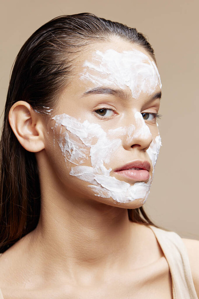 Gyönyörű nő alkalmazása nyugtató arc maszk bőrápolás bézs háttér - Fotó, kép