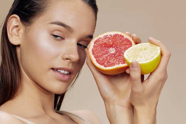 mooie vrouw grapefruit met citroen in handen glimlach vitaminen beige achtergrond - Foto, afbeelding