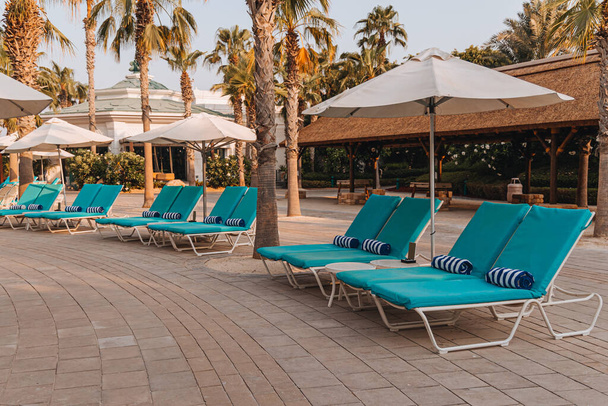 Piscina con cama azul y toalla bajo sombrillas abiertas sobre el telón de fondo de hermosas palmeras, descanso, vacaciones, relajación - Foto, imagen