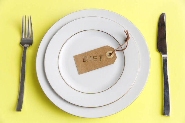Serving two plates, spoon, fork, knife on the yellow background. The concept of weight loss and diet. The concept of weight loss and diet. Label with the inscription - diet in an empty plate - Zdjęcie, obraz