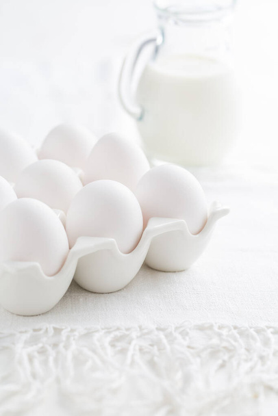 Leche ecológica y huevos frescos en mesa de cocina blanca - Foto, imagen