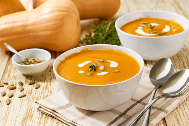 Delicious pumpkin soup in bowl with cream sauce on a white wooden table, selective focus. - Foto, immagini