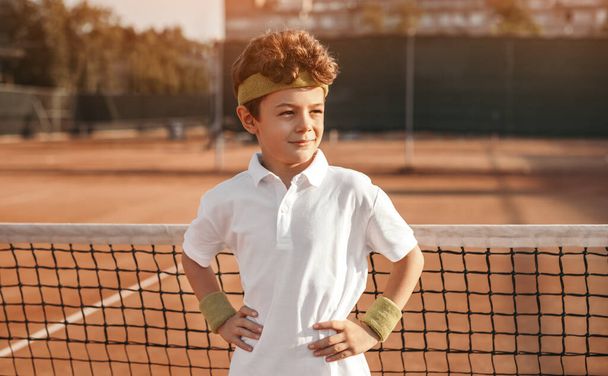 Confident little boy standing on tennis court and looking away - Fotoğraf, Görsel