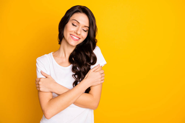 Portrait of pretty dreamy cheerful girl hugging herself enjoying copy space isolated over bright yellow color background - Φωτογραφία, εικόνα