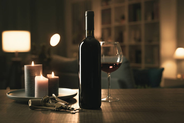 Hervorragende Rotweinverkostung: Flasche, Weinglas, brennende Kerzen und Korkenzieher auf einem Tisch im Wohnzimmer - Foto, Bild