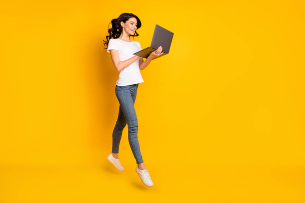 Photo of adorable sweet young woman wear white t-shirt jumping holding modern device empty space isolated yellow color background - Valokuva, kuva