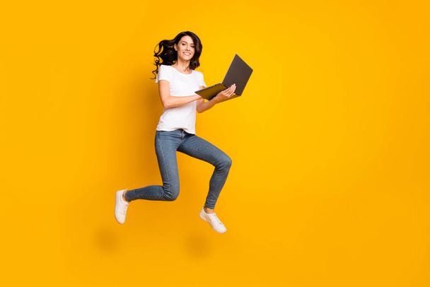 Повнометражний вигляд на тіло прекрасної веселої дівчини, що стрибає з використанням успіху ноутбука ізольовано на яскравому жовтому кольоровому фоні
 - Фото, зображення
