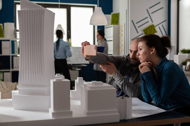 ビデオ通話会議でスマートフォンを使用している2人の建築家の同僚のチーム - 写真・画像